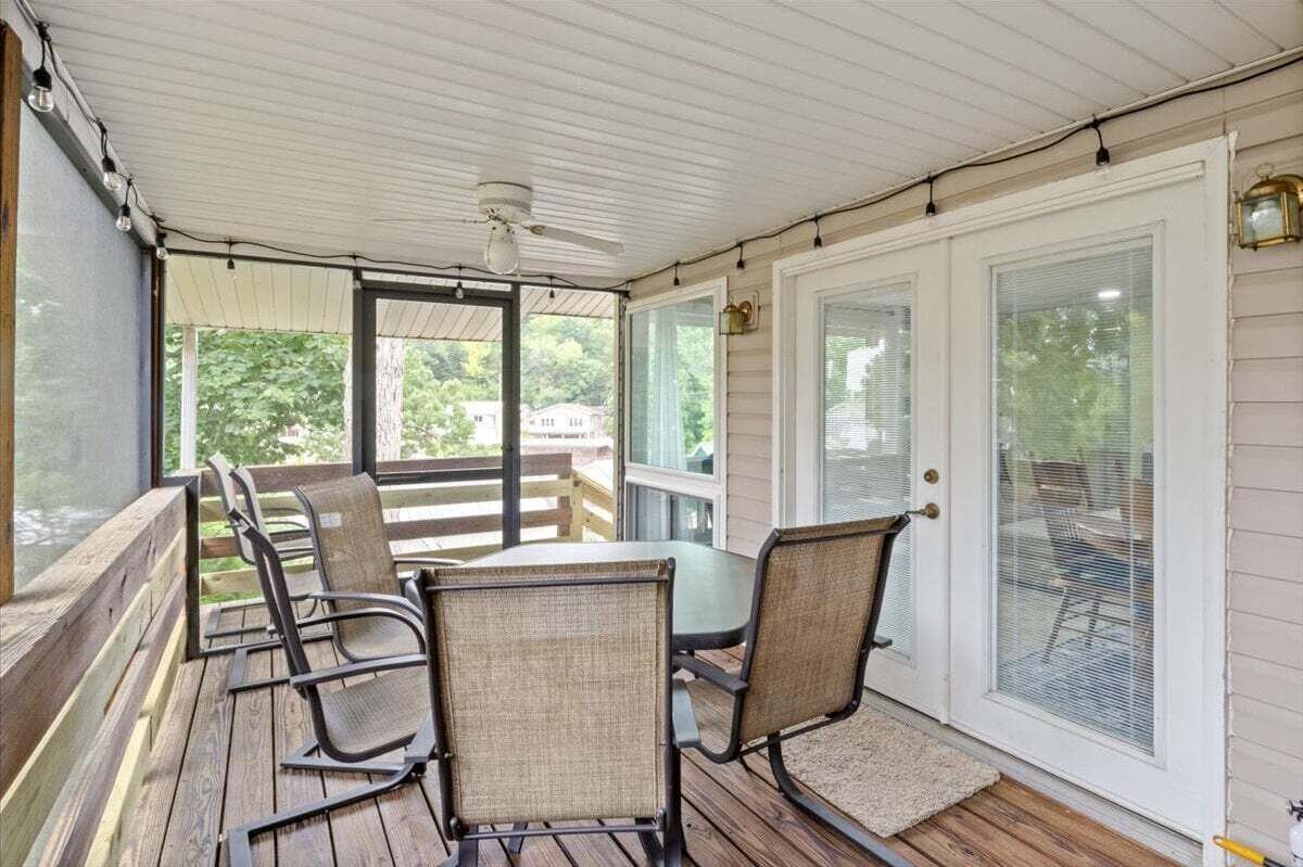 Een overdekt terras met een tafel, stoelen, een plafondventilator en uitzicht op de omgeving.