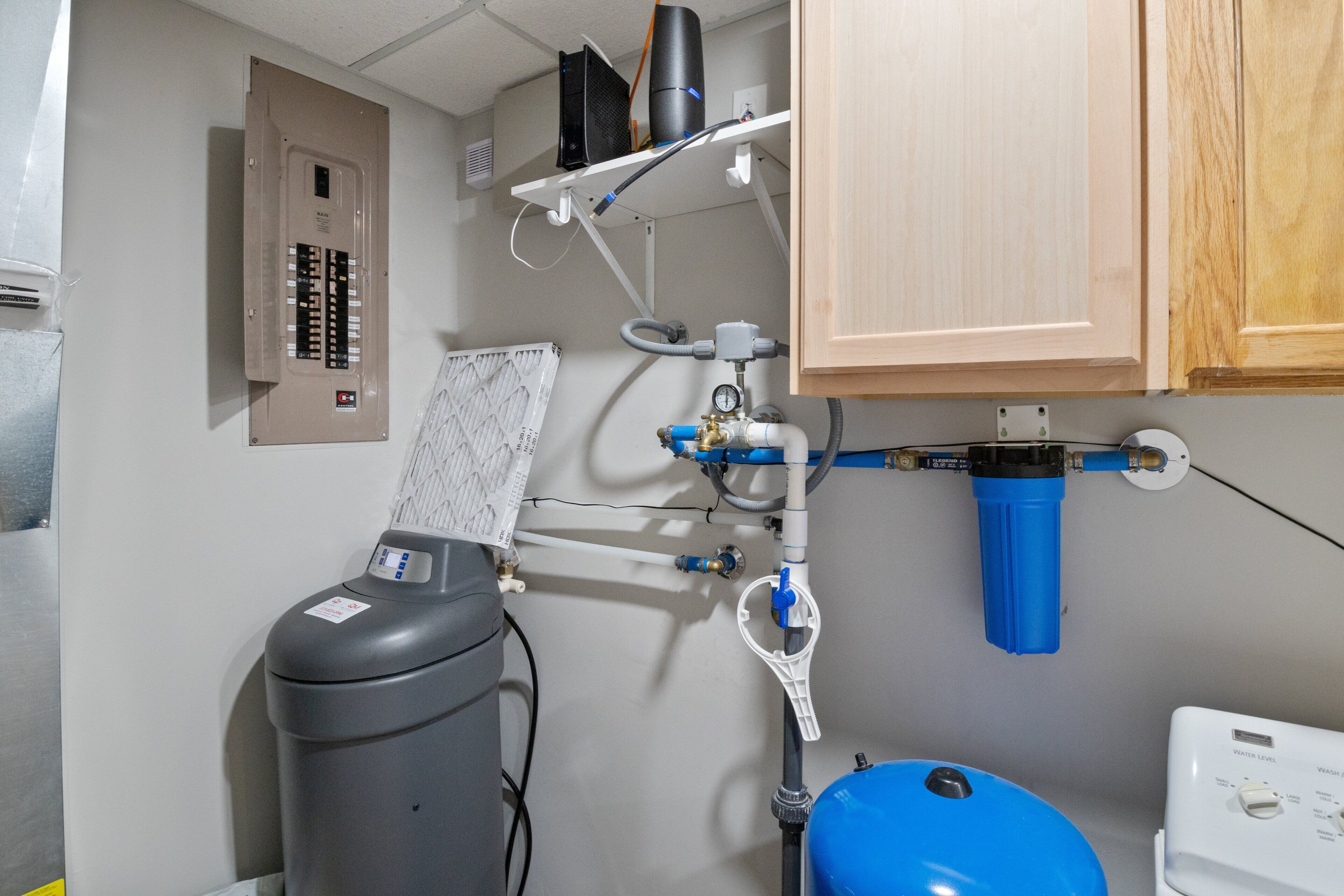 A bathroom with a water heater, a blue water tank, and a control panel.