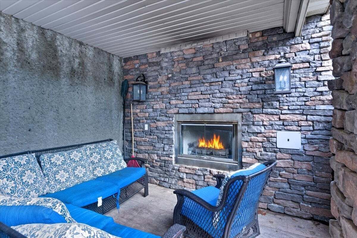 A stone-walled outdoor seating area with a fireplace, blue cushions, and wicker furniture.