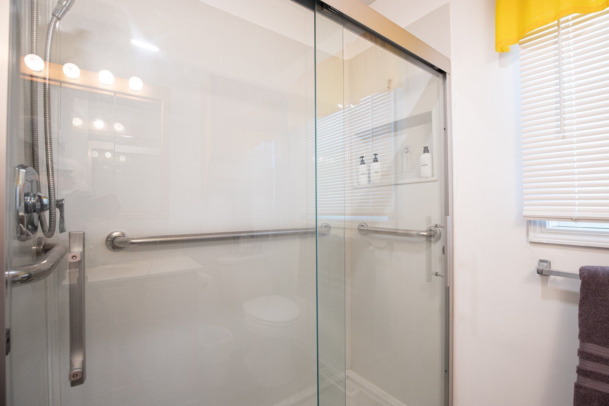 Une salle de bain moderne dotée d’une cabine de douche en verre, d’une barre d’appui et d’un porte-serviettes.