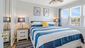 Un dormitorio con una cama grande, dos lámparas de noche, un ventilador de techo y dos cuadros con motivos de pájaros.
