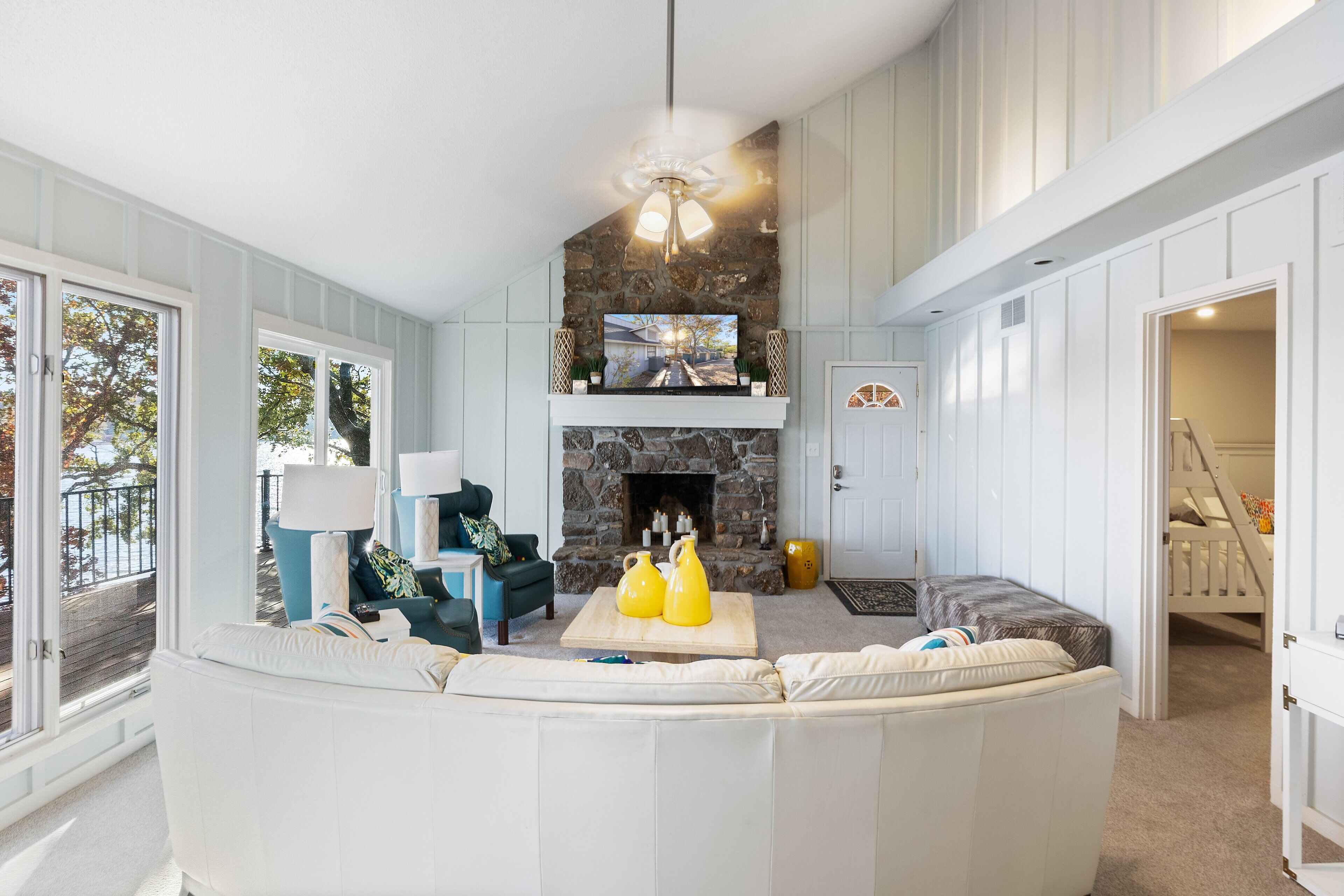 A living room with a stone fireplace, a large white sofa, and a television above the fireplace.