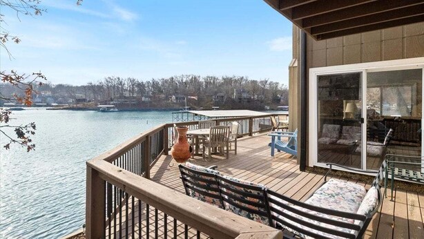 A deck with outdoor furniture, a large window, and a view of a body of water and distant buildings. - Expansive Deck, Beautiful Views, Private Dock & Boat Slip (Sunrise Beach)