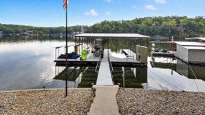 A dock with a covered seating area, a flag, and a view of the lake. - Expansive Deck, Beautiful Views, Private Dock & Boat Slip (Sunrise Beach)
