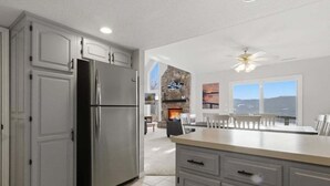A modern kitchen with grey cabinetry, a stainless steel refrigerator, and a dining area with a view. - Expansive Deck, Beautiful Views, Private Dock & Boat Slip (Sunrise Beach)