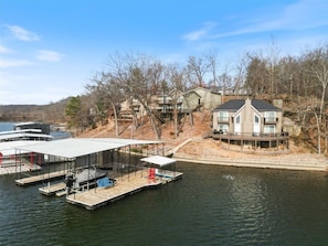 A waterfront property with a dock, a covered boat launch, and a house with a large deck. - Expansive Deck, Beautiful Views, Private Dock & Boat Slip (Sunrise Beach)