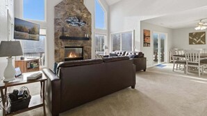 A spacious living room with a stone fireplace, a large window, a sofa, and a dining area. - Expansive Deck, Beautiful Views, Private Dock & Boat Slip (Sunrise Beach)