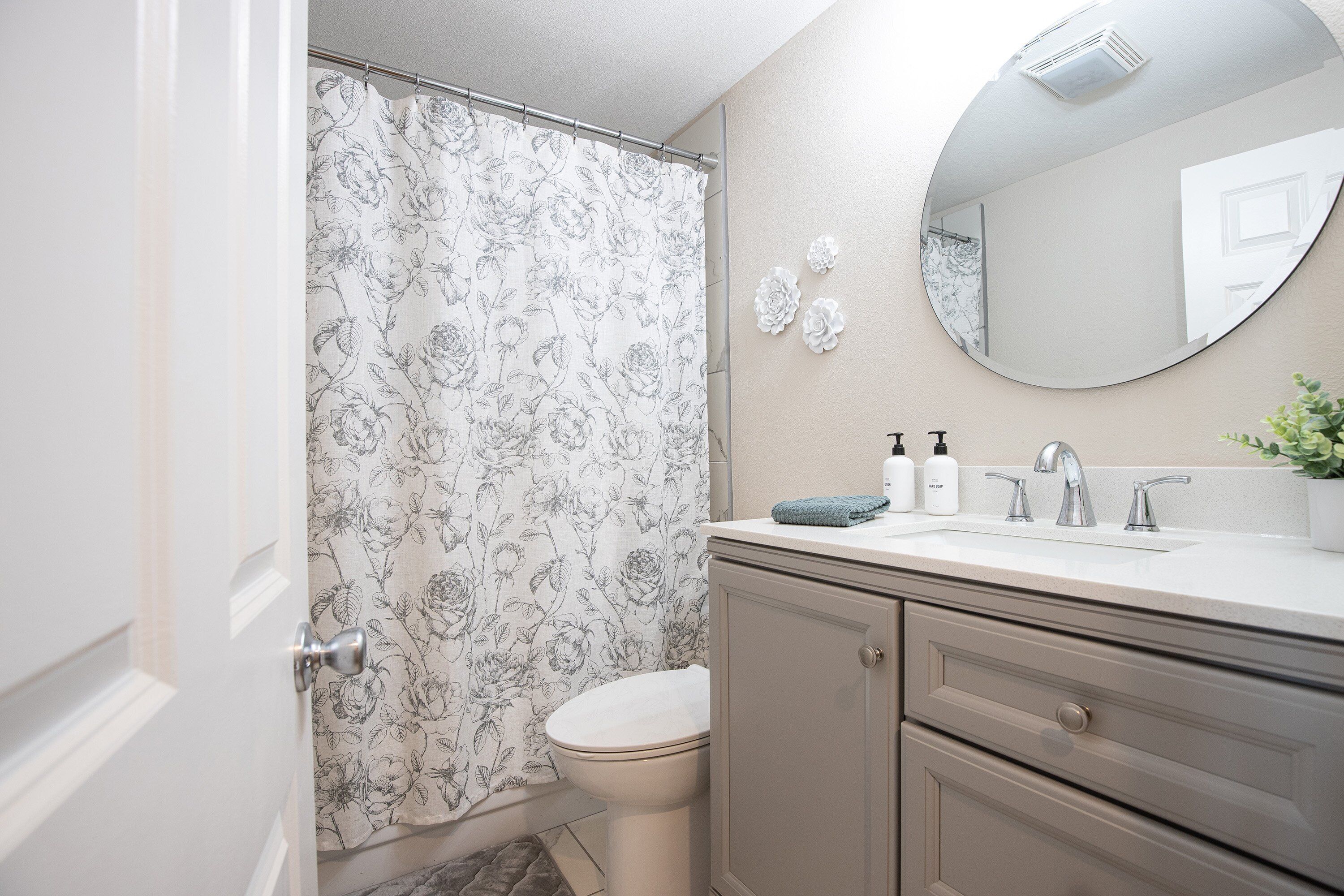 A bathroom with a toilet, a sink with a mirror, and a shower curtain with a floral pattern.