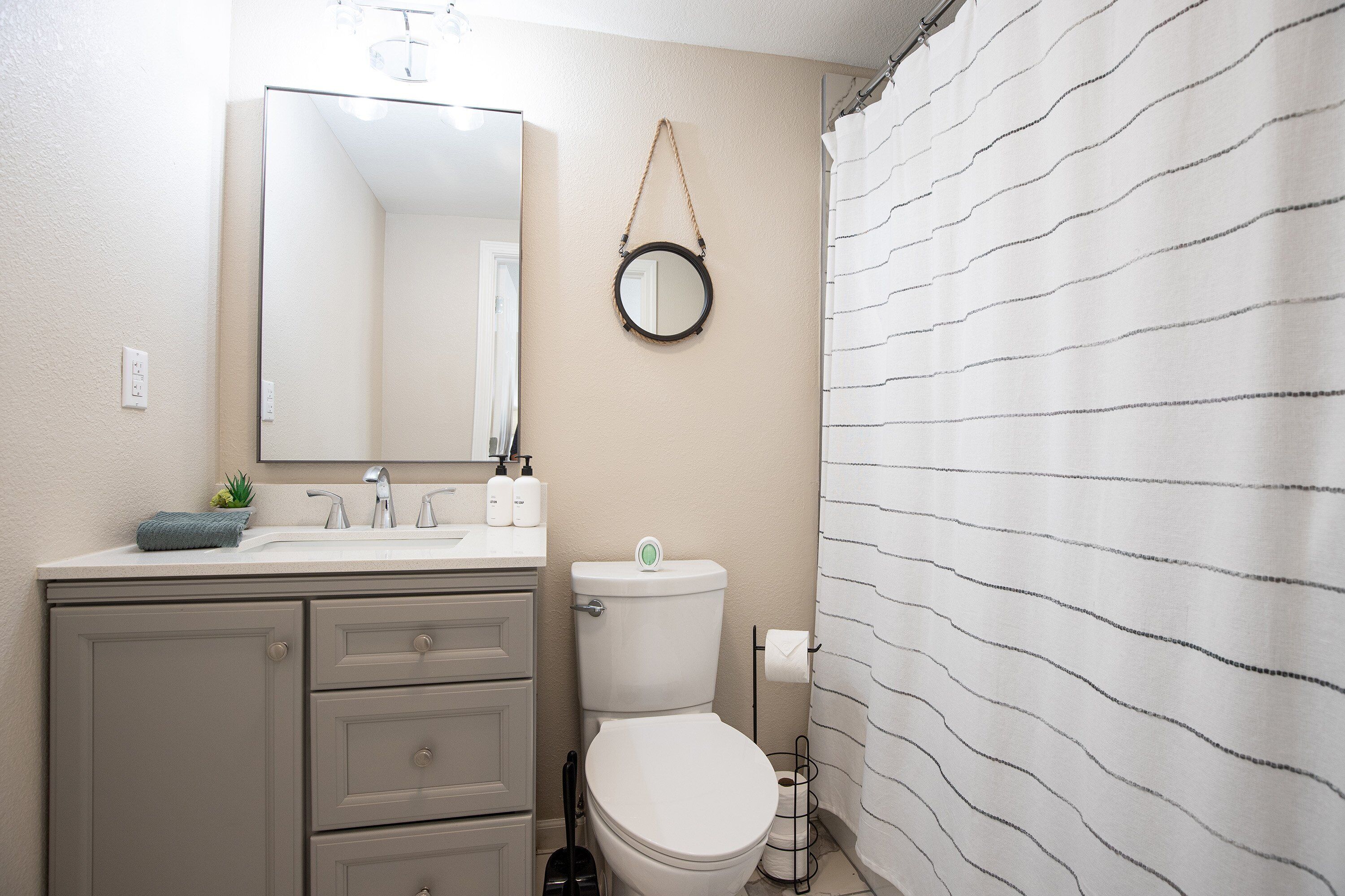 Une salle de bain avec des toilettes, un lavabo et un miroir. Il y a une serviette et une petite plante sur le comptoir.