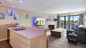 Uma sala de estar moderna com área de cozinha, lareira e uma grande janela com cortinas.