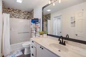 Et moderne badeværelse med badekar, toilet og vask. Der er et spejl over vasken og en badeforhæng.