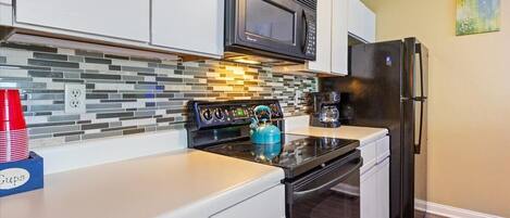 A kitchen with white cabinets, a black microwave, a stainless steel stove, and a black refrigerator.