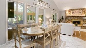 Un comedor amplio con una mesa redonda y sillas de madera, ventanas grandes y una chimenea de piedra.