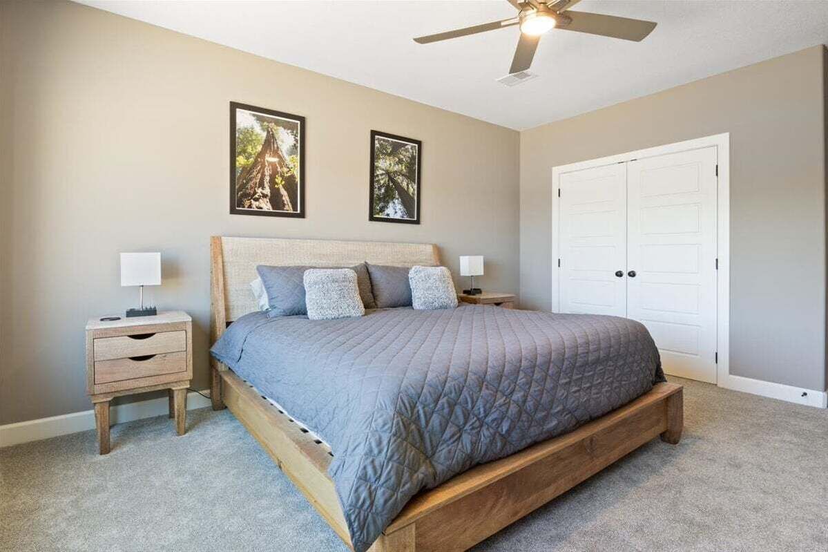 A bedroom with a bed, two nightstands, a ceiling fan, and a door.