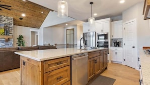 Une cuisine moderne avec des meubles en bois, un îlot central, des appareils en acier inoxydable et des luminaires suspendus.