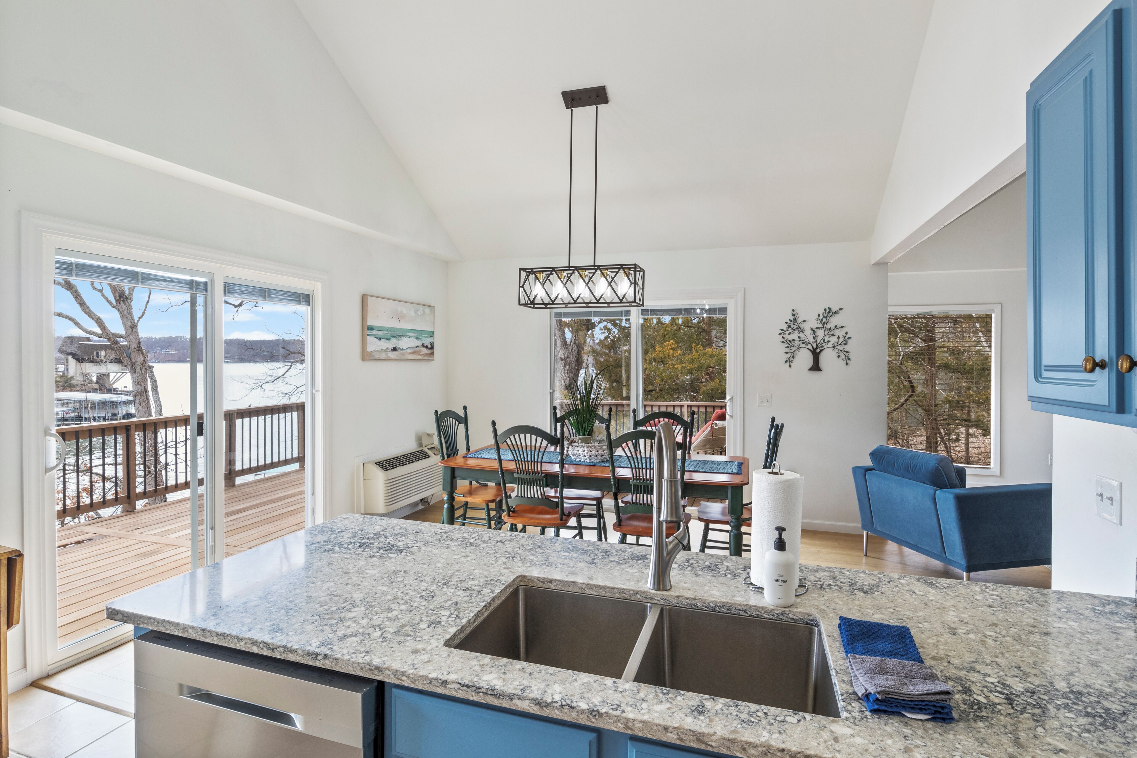 A modern kitchen with a large island, a dining area with a wooden table and chairs, and a blue sofa.