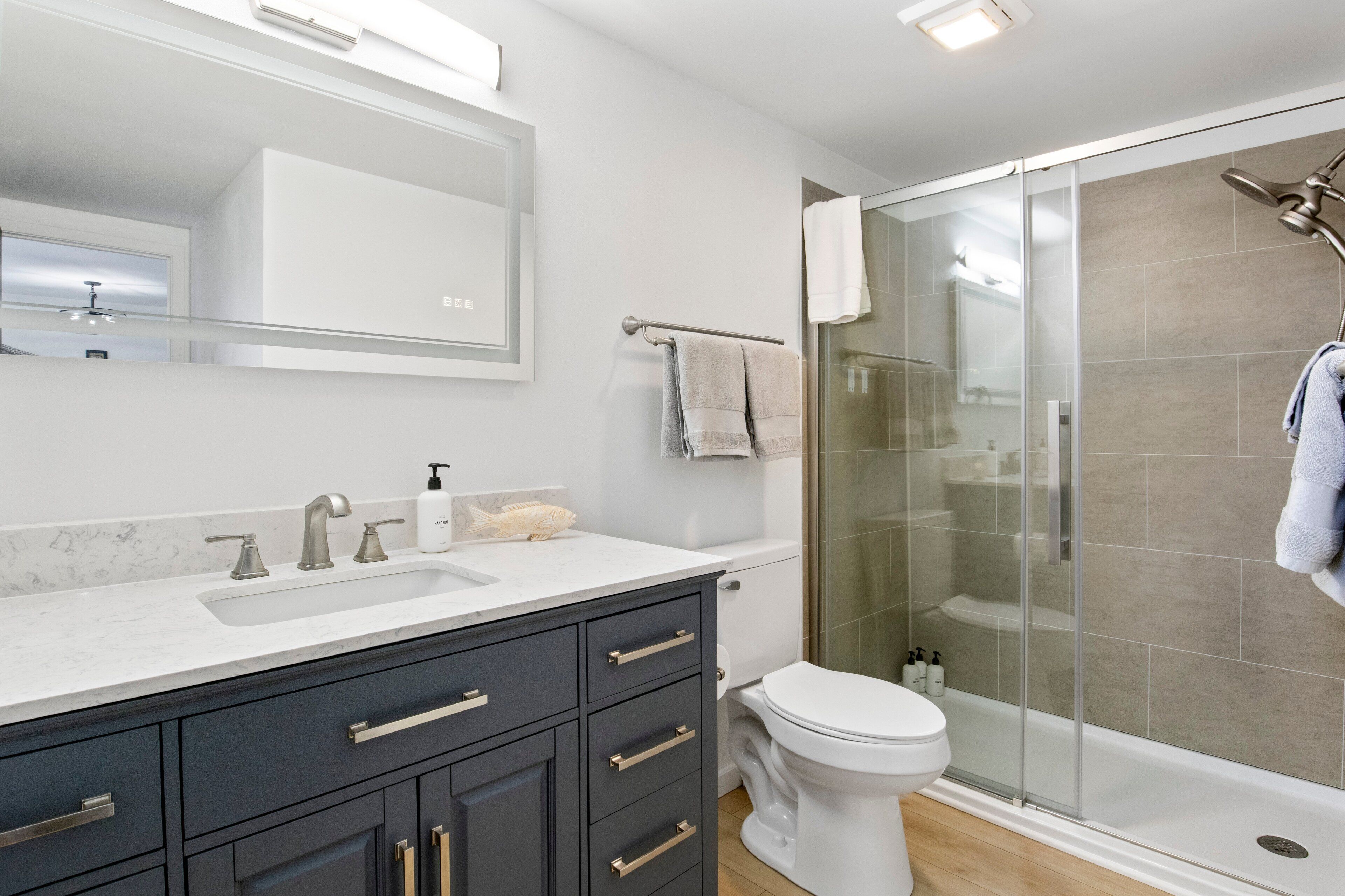 A modern bathroom with a glass-enclosed shower, a white sink with a marble countertop, and dark cabinetry.