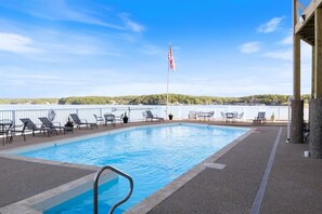 A swimming pool with lounge chairs and a flag, surrounded by a railing and a view of a lake. - Lakeview Condo w/ 2 Pools & Beach - Family Fun Awaits at 21mm (Osage Beach)