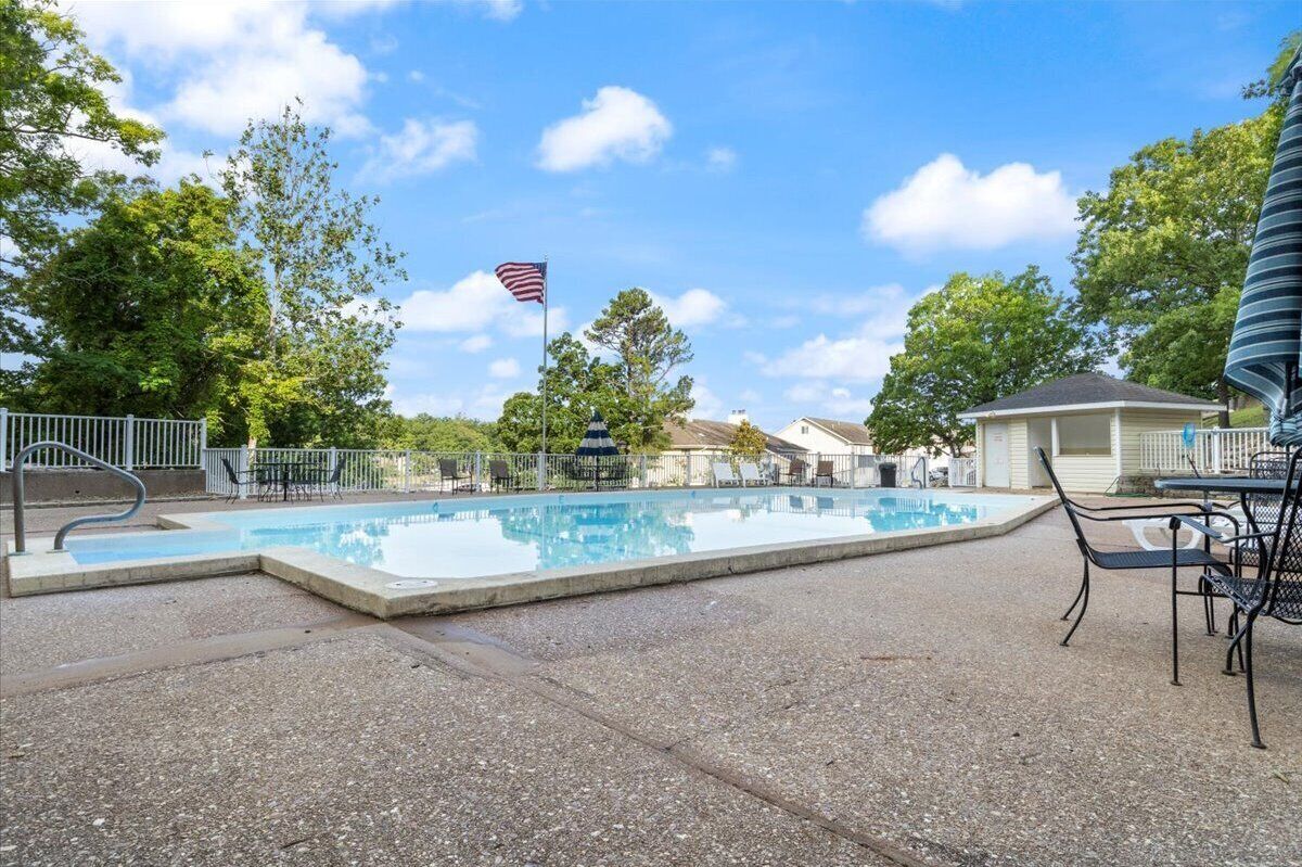 A swimming pool with a flag, surrounded by trees and a gazebo.