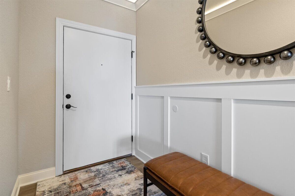A hallway with a white door, a bench, and a wall-mounted mirror with a decorative frame.