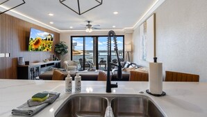 A modern kitchen with a built-in sink, a dining area with a view, and a living room with a sofa and a TV.