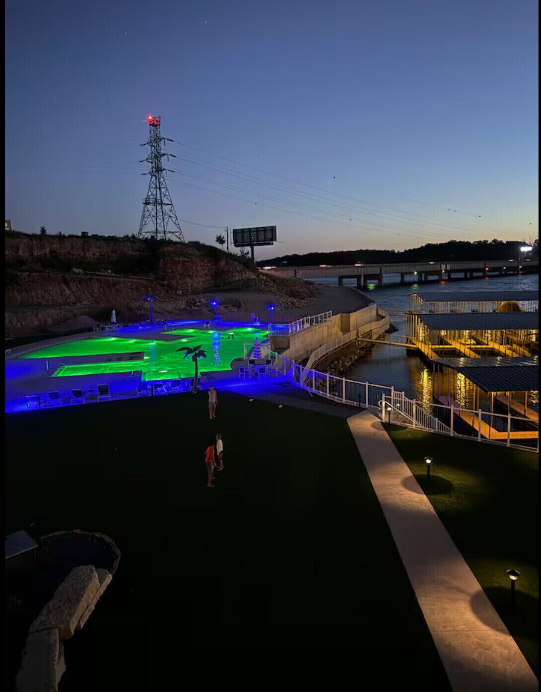 A nighttime view of a waterfront area with illuminated pathways and a sports field.