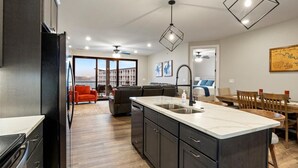 A modern kitchen with a central island, dark cabinetry, and a dining area with wooden chairs. - Family-fun Lakeside Luxury at Topsider in Osage w/ 2 Pools, Prime Views Pack N' Play & Games (Osage Beach)