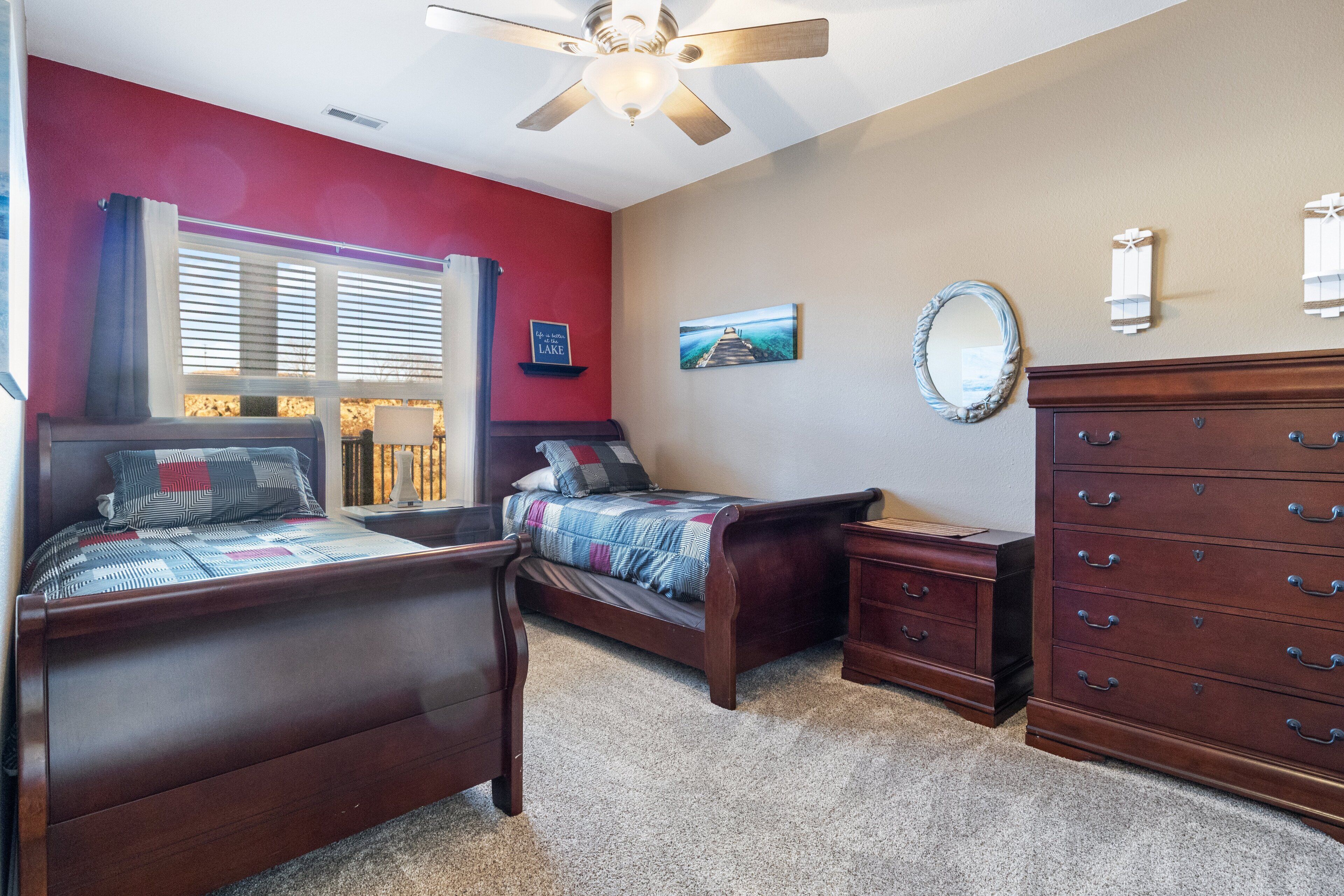 A bedroom with two wooden beds, a dresser, a ceiling fan, and a painting on the wall.