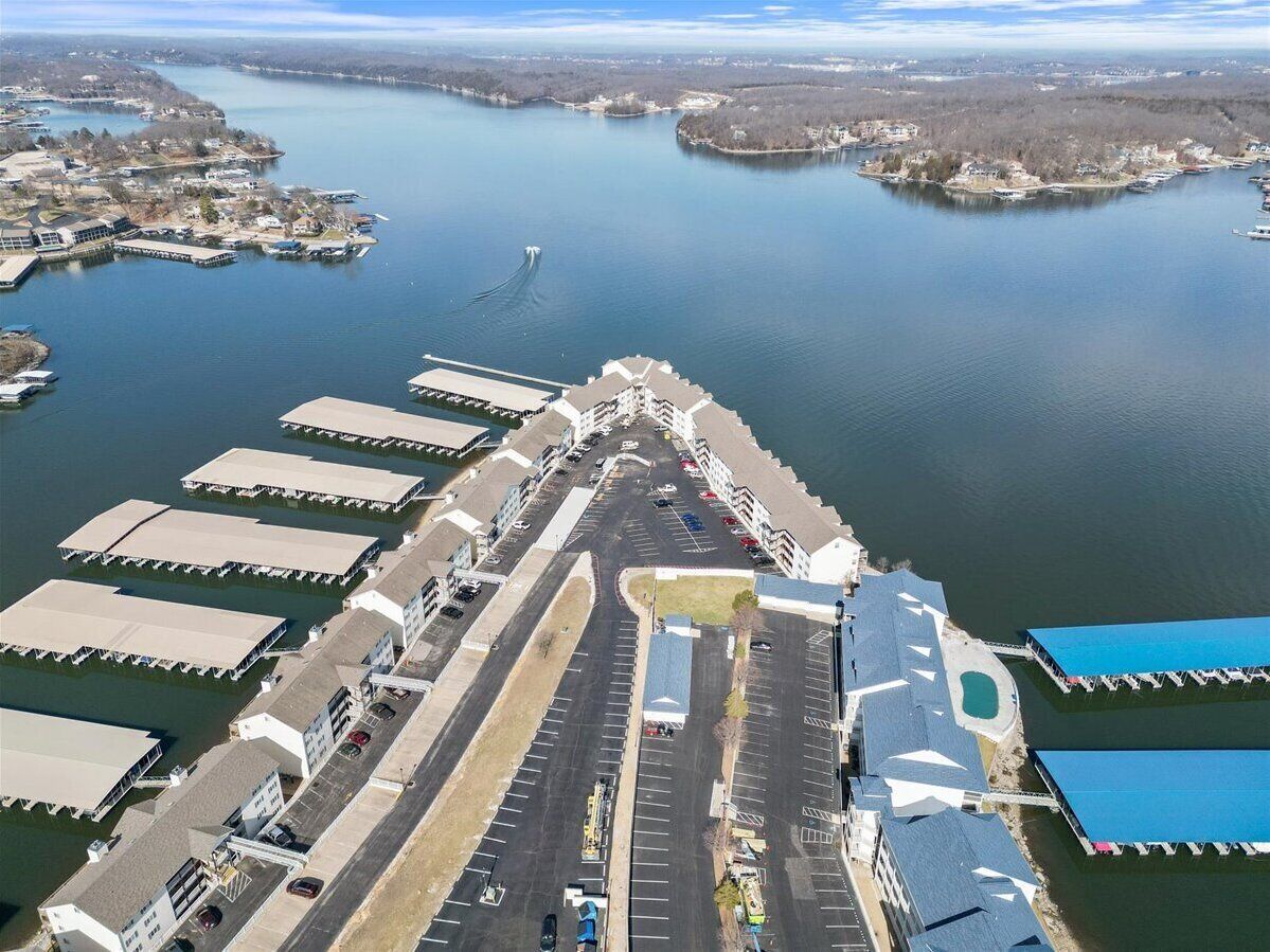 Une vue aérienne d’une marina où sont amarrés des bateaux, d’un parking et d’un grand bâtiment doté d’un toit remarquable.
