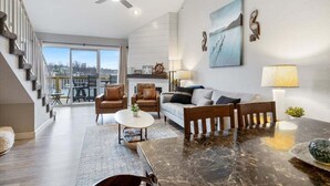 A modern living room with a sofa, chairs, a coffee table, and a dining table. There is a staircase on the left, a large window with a view, and a ceiling fan. - Family-perfect Lakefront Fun at The Ledges, 21mm, 2 Pools & Beach (Osage Beach)
