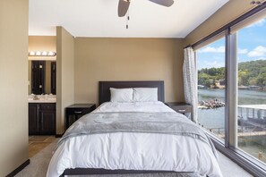 A bedroom with a large bed, a ceiling fan, a view of a lake, and a bathroom with a vanity and mirror. - Stunning Views, Inviting Pools, and Endless Fun! (Osage Beach)