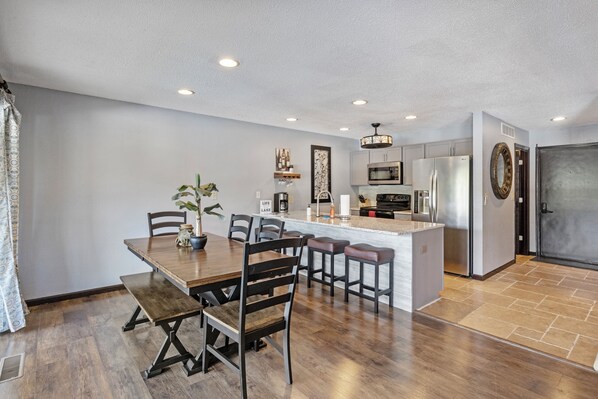 A modern kitchen with a central island, stainless steel appliances, and a dining area with wooden furniture. - Stunning Views, Inviting Pools, and Endless Fun! (Osage Beach)