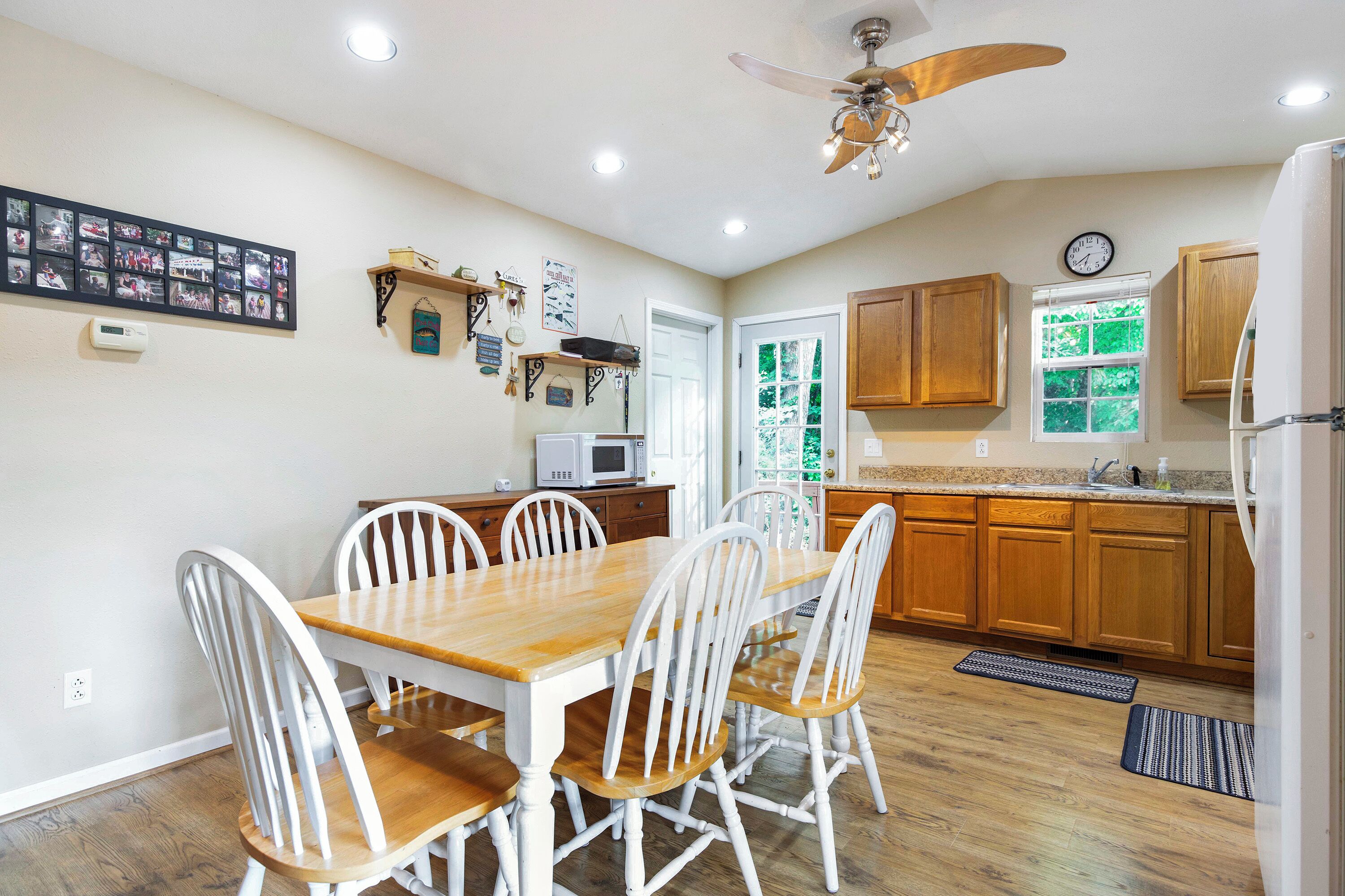 A dining area with a wooden table and white chairs, a ceiling fan, and wooden cabinets.