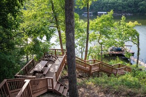 A wooden deck with picnic tables and a staircase leading to a dock by a lake. - Lake Cabin & Dock - A True Ozarks Experience! (Barnett)