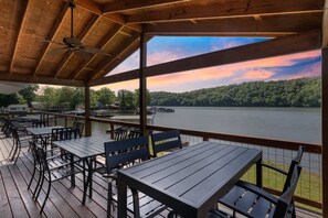 An outdoor deck with tables and chairs, overlooking a lake and forested hills.