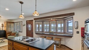 A kitchen with a large island, wooden cabinets, and a window overlooking a scenic view. - 17 Lakefront Acres, Private Dock, Firepit, Pool Table, Kayaks, Fishing (Gravois Mills)