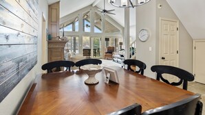 A dining area with a wooden table, chairs, a chandelier, and a view of the outdoors through large windows. - Family-friendly, Dock Enjoyment, Kayaks, Lake View (Sunrise Beach)