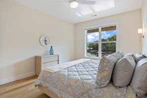 Een slaapkamer met een bed, een raam, een plafondventilator en een nachtkastje met een vaas.