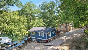 A blue house with a dock, surrounded by trees and a gravel driveway. - Minutes From the Strip - Nightlife and Dining! (Lake Ozark)