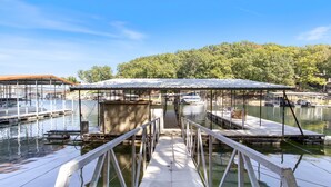 A dock leading to a covered boat house with a view of the water and trees in the background. - Minutes From the Strip - Nightlife and Dining! (Lake Ozark)