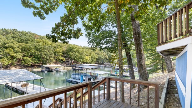A wooden deck overlooking a marina with boats docked, surrounded by trees and hills. - Minutes From the Strip - Nightlife and Dining! (Lake Ozark)