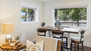 A cozy living room with a wooden chair, a dining table, and a chandelier. There are windows with views of trees and a fence. - Minutes From the Strip - Nightlife and Dining! (Lake Ozark)