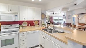 A modern kitchen with white cabinets, a microwave, an oven, and a dishwasher. There is a red accent wall, a sink, and a dining area visible in the background. - Prime Spot, Breathtaking Views, Nearby Attractions (Lake Ozark)
