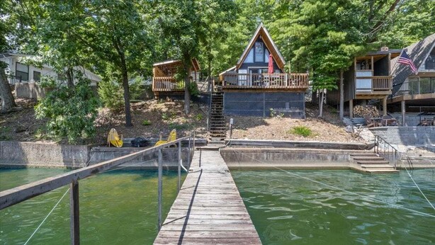 A wooden dock leading to a house with a deck, surrounded by trees and a body of water. - Pet Friendly A Frame w/ Private Dock & Great Lake Views (Rocky Mount)