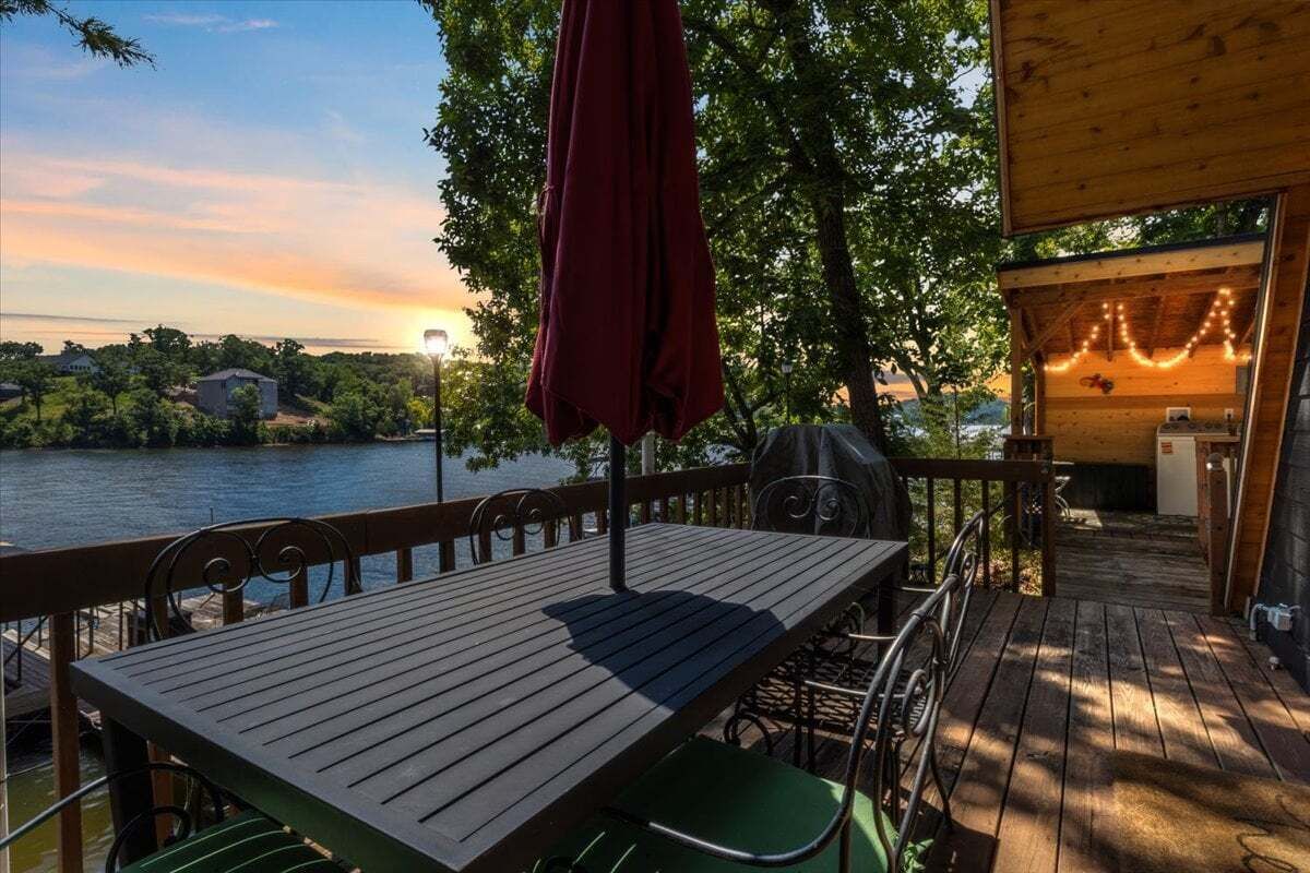 A wooden deck with a table and chairs, overlooking a body of water and trees.