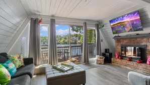 A spacious living room with a large TV, a fireplace, and a view of a lake. - Pet Friendly A Frame w/ Private Dock & Great Lake Views (Rocky Mount)