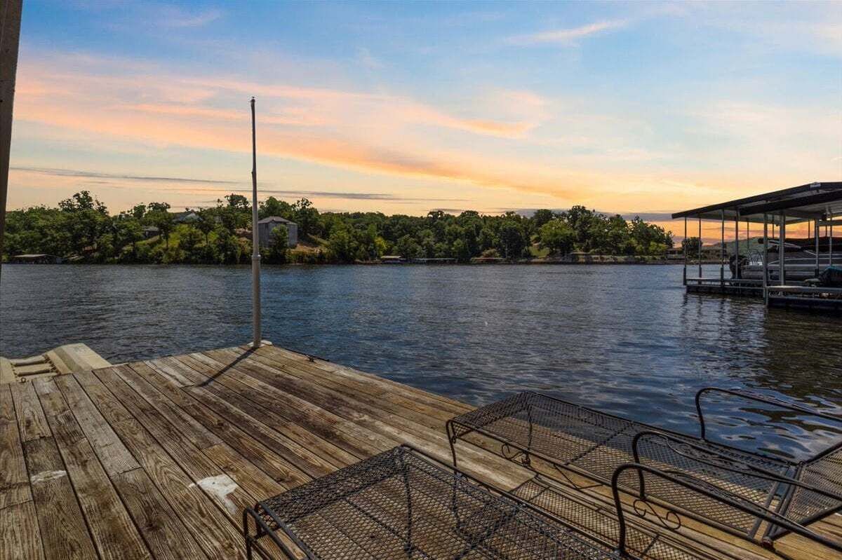A wooden dock with metal chairs and a covered area extending over water.
