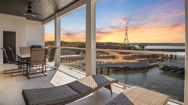 Un balcon doté d’un ensemble de mobilier de jardin et de chaises en osier, offrant une vue sur une rivière et un pont.