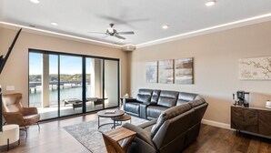 Un salon moderne avec un canapé en cuir, une table basse et une vue sur un plan d’eau, visible à travers de grandes portes-fenêtres coulissantes.