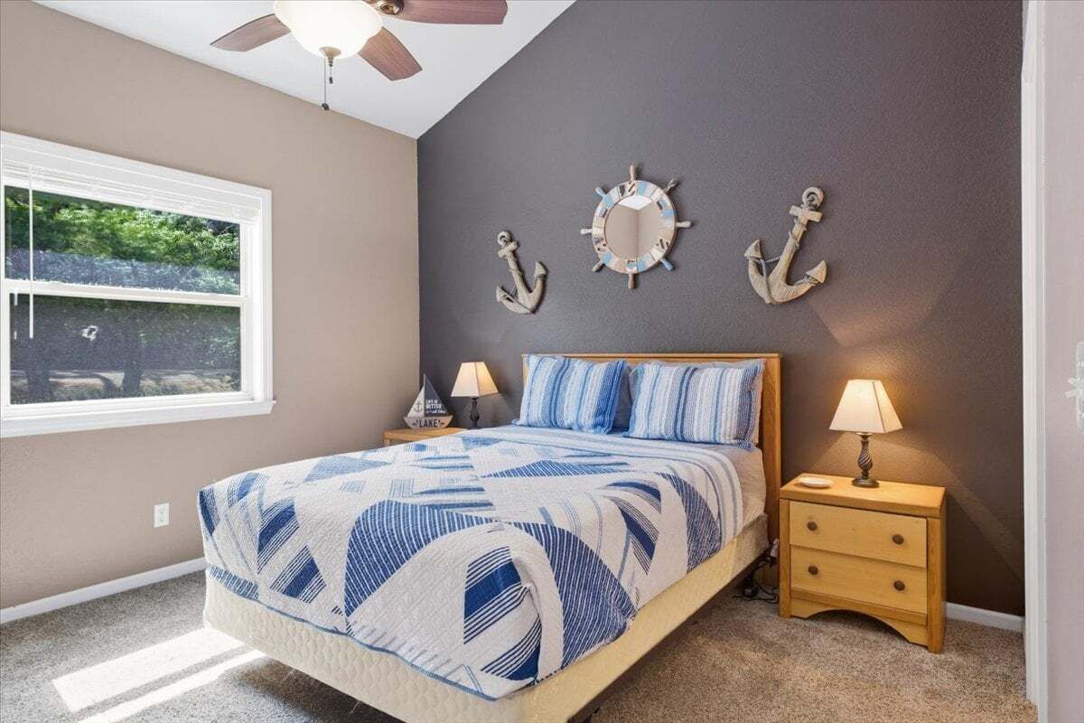 A bedroom with a bed, two nightstands, a ceiling fan, a window, and wall decorations including anchors and a clock.